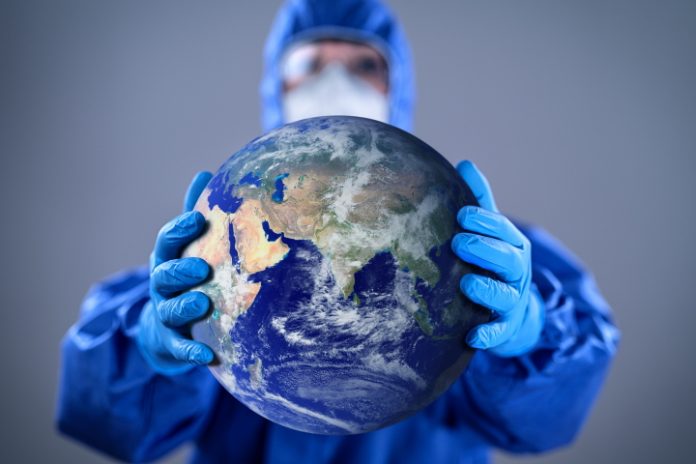 De aardbol in handen van een medicus met mondmasker en volledig beschermde kleding