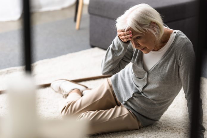senior woman with migraine sitting on carpet and touching forehead with hand