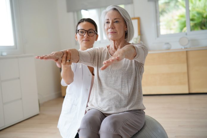 Senior woman exercising with her physiotherapist and swiss ball