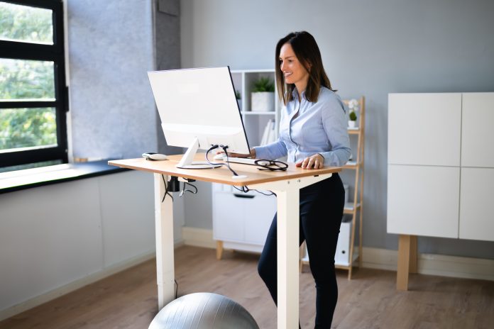 Woman Using Adjustable Height Standing Desk In Office