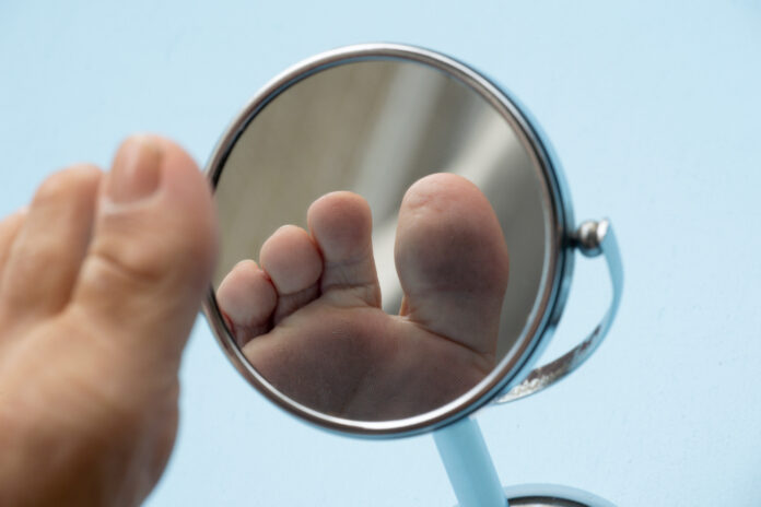 Person looking at the sole of the foot in a mirror. Person looking at the sole of the foot in a mirror, to check if there is no diabetic foot, as possible sores